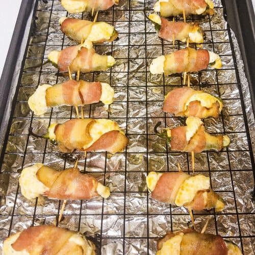 bacon wrapped jalapenos on a wire rack going into the oven