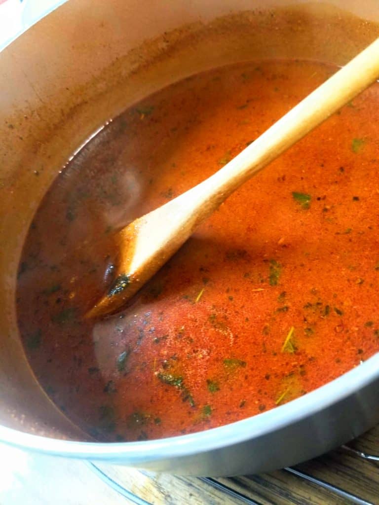 red enchilada sauce with a wooden spoon in a pan. 